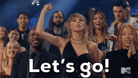 Auf dem Bild ist Taylor Swift zu sehen, die vor einer Menge anderer Menschen ihre Faust reckt davor eine Aufschrift mit "Let's Go!"